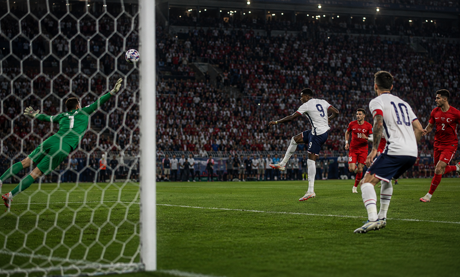 USA forward unleashes a long-range shot against Turkey as the goalkeeper dives, with teammates watching under floodlit stadium lights.