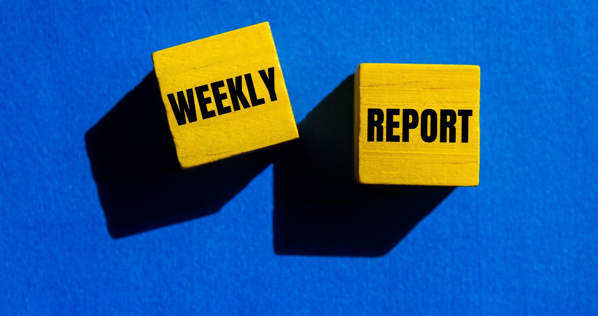 Two wooden blocks are face up facing the camera. One says weekly the other says report.