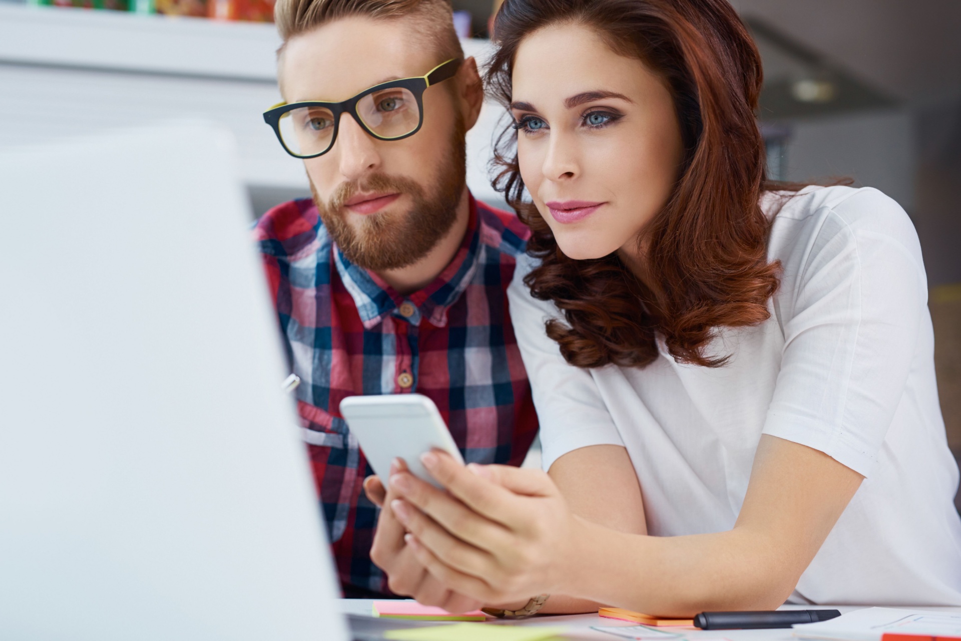 Young couple on phone while also looking at a computer screen