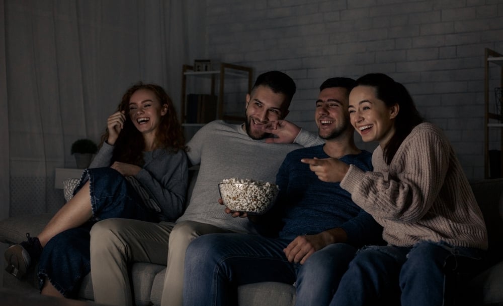 group of friends sitting on sofa watching tv