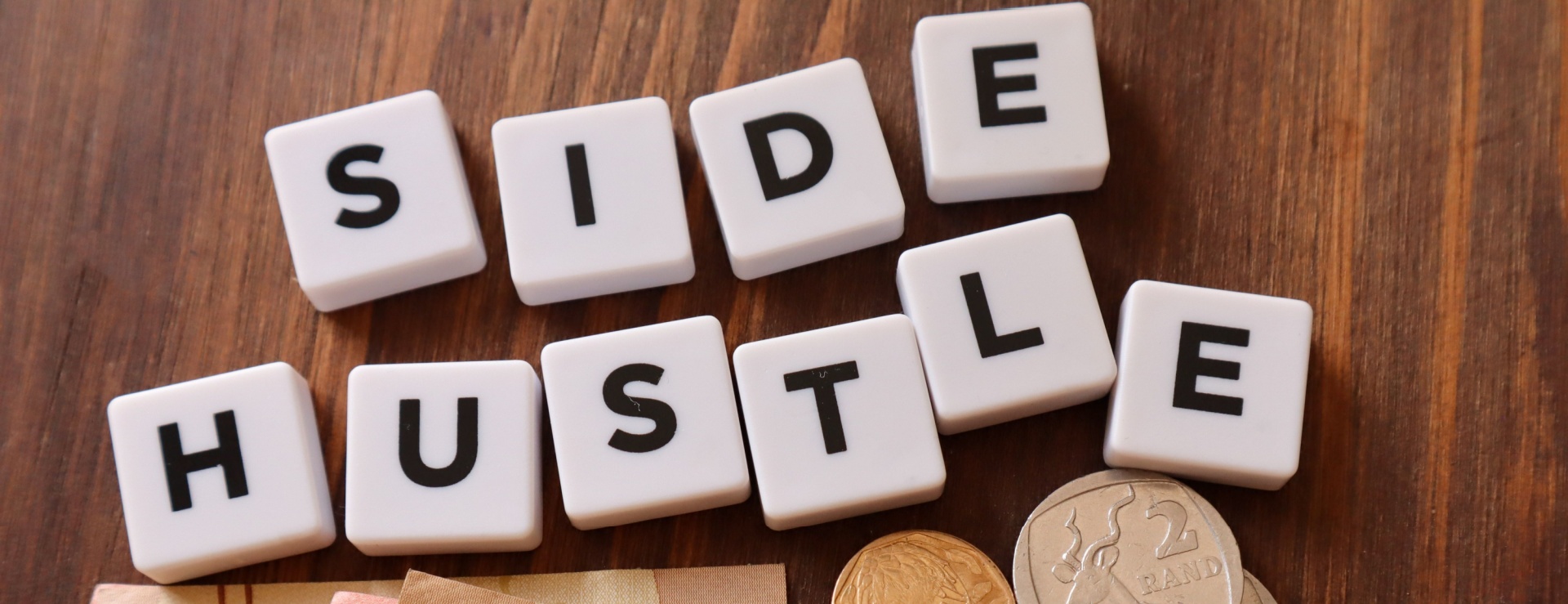 Side hustle in scrabble letters with coins and notes all around it. 