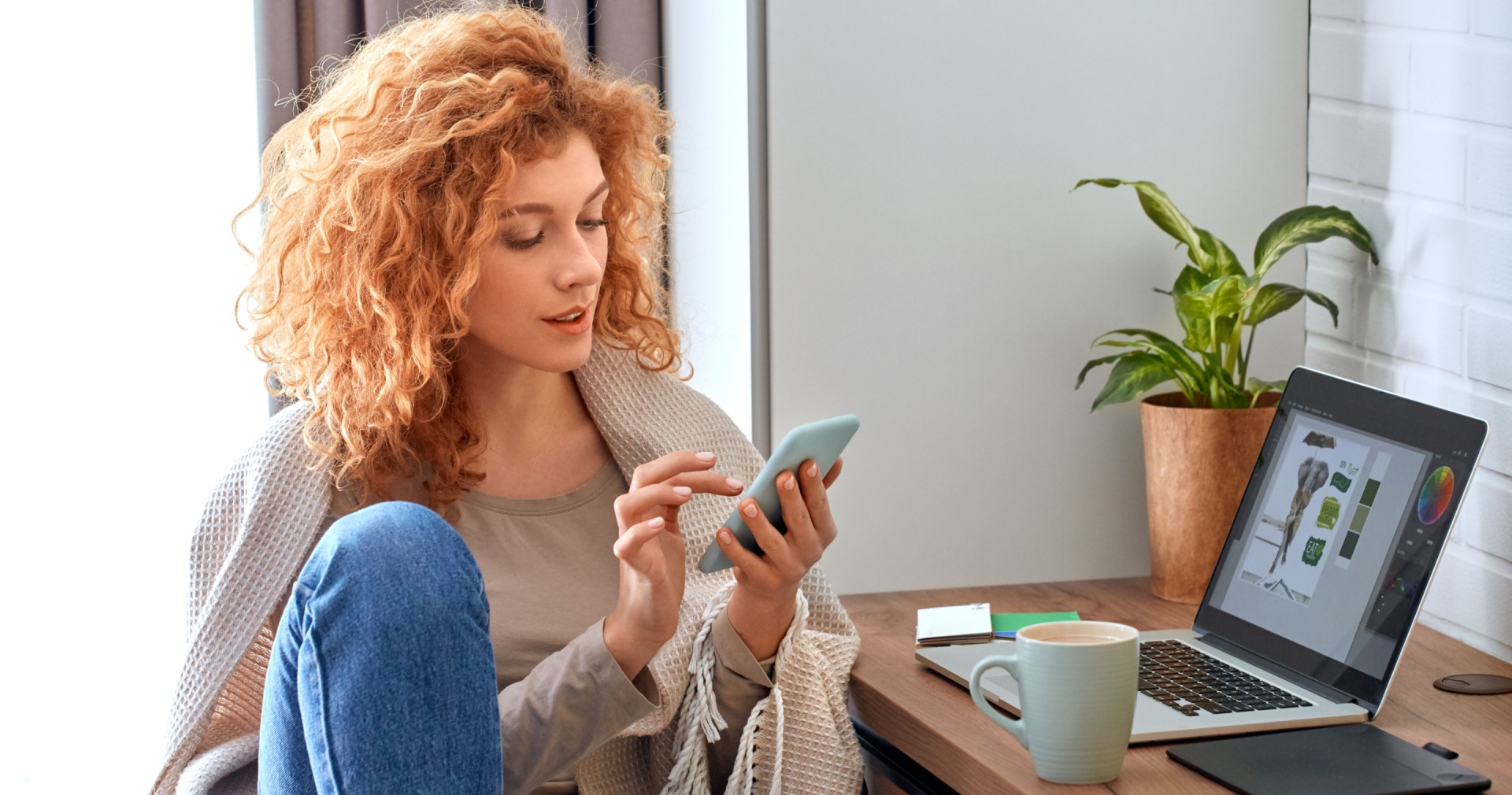 Woman sat on phone while there is a laptop on her desk